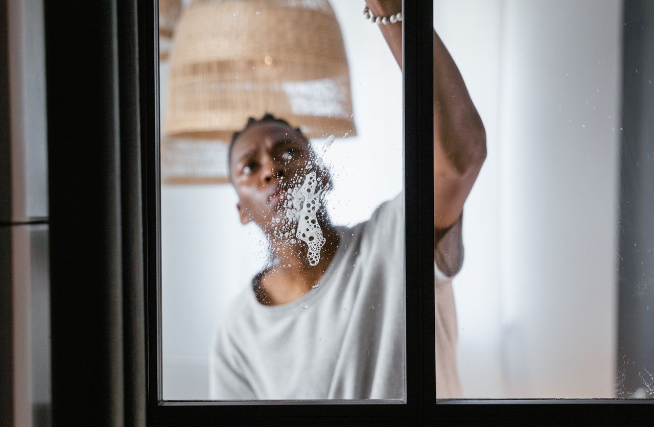 contact-img An adult male cleaning a glass window indoors, focusing on household chores and cleanliness.